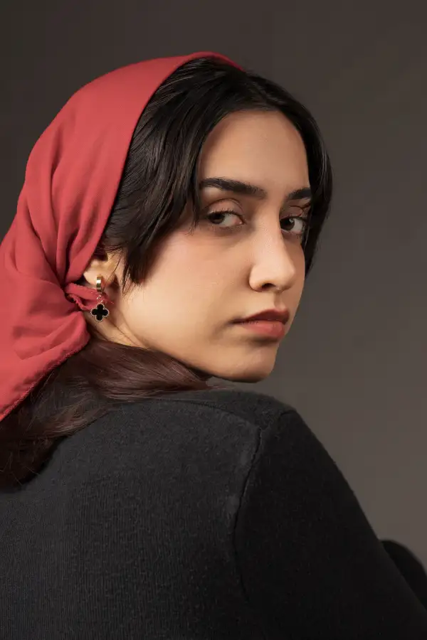 پرتره‌ی استودیویی با نگاهی نافذ به دوربین؛ تاکید بر کنتراستِ رنگ گرم پوشش سر با نورپردازی کنترل‌شده‌ی چهره.