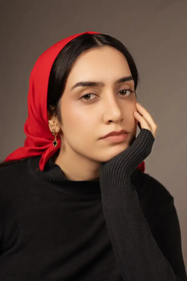 پرتره استودیویی با نگاه متفکر و نور نرم، با پوشش سر قرمز و پس‌زمینه خنثی.